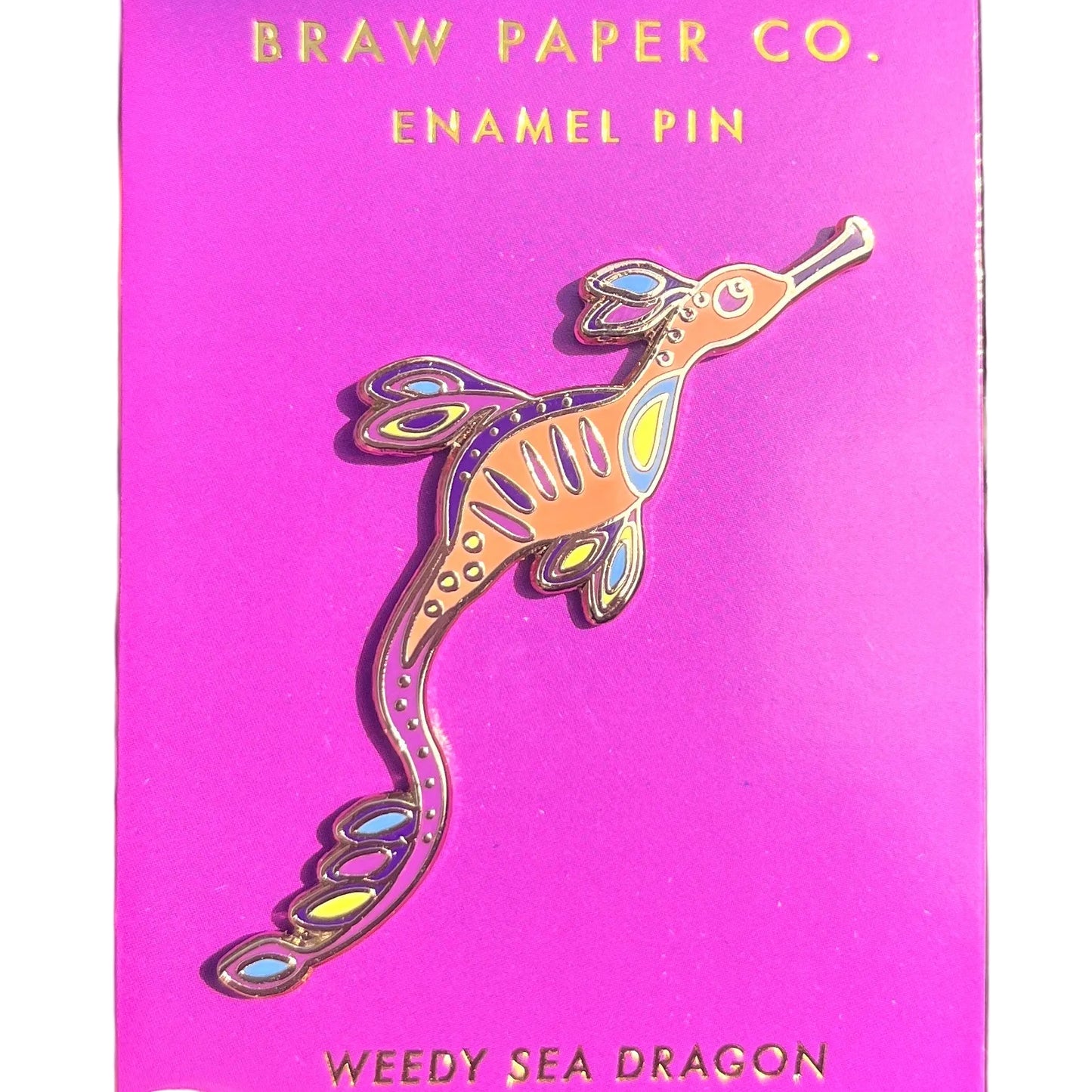 Enamel pin of a weedy sea dragon on a purple card with 'Braw Paper Co.' branding,