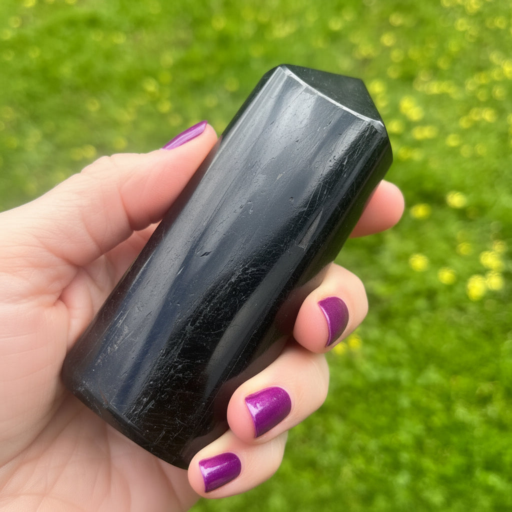 Hand holding a black tourmaline crystal against a green outdoor background