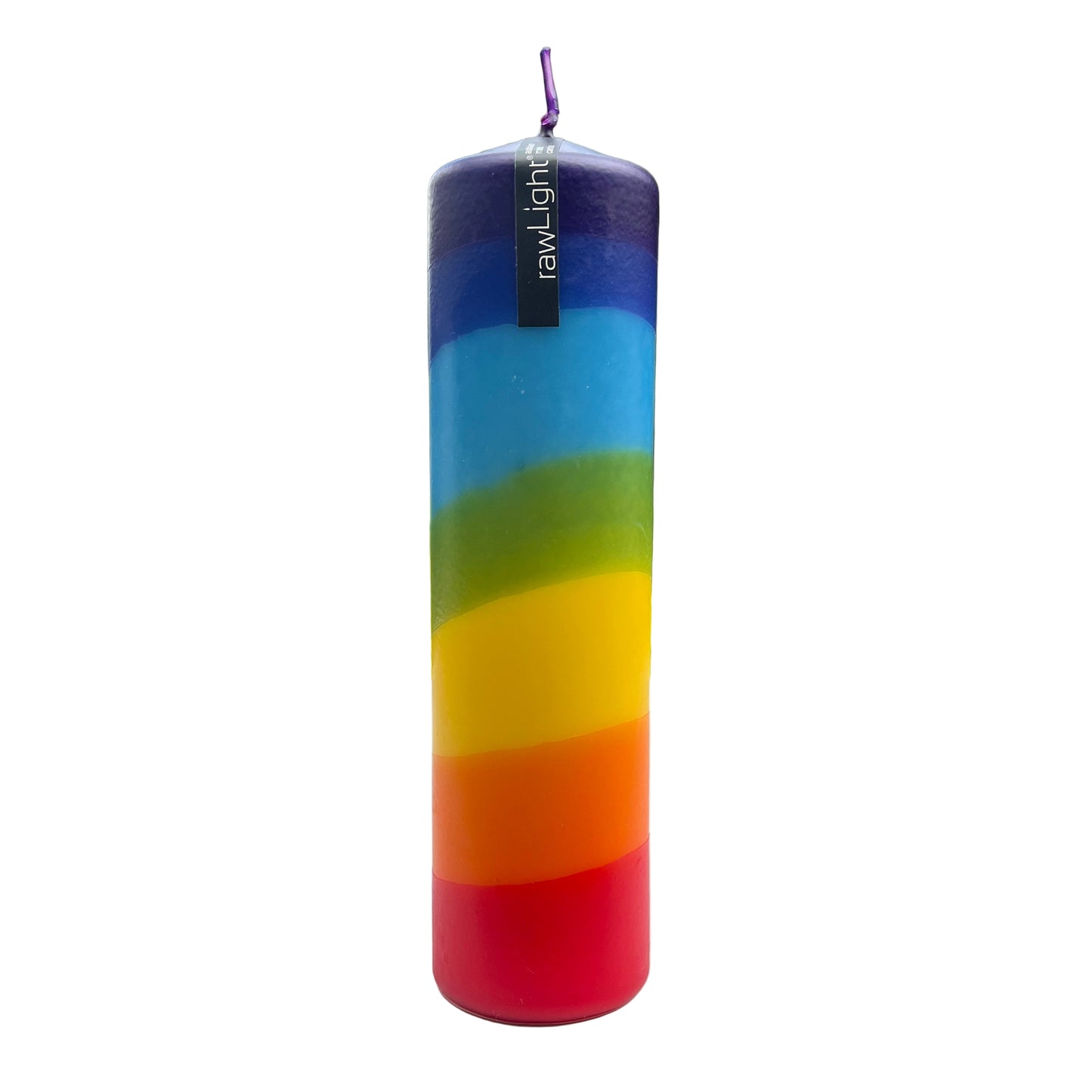 Colorful cylindrical candle with rainbow pattern on a white surface, blurred outdoor background