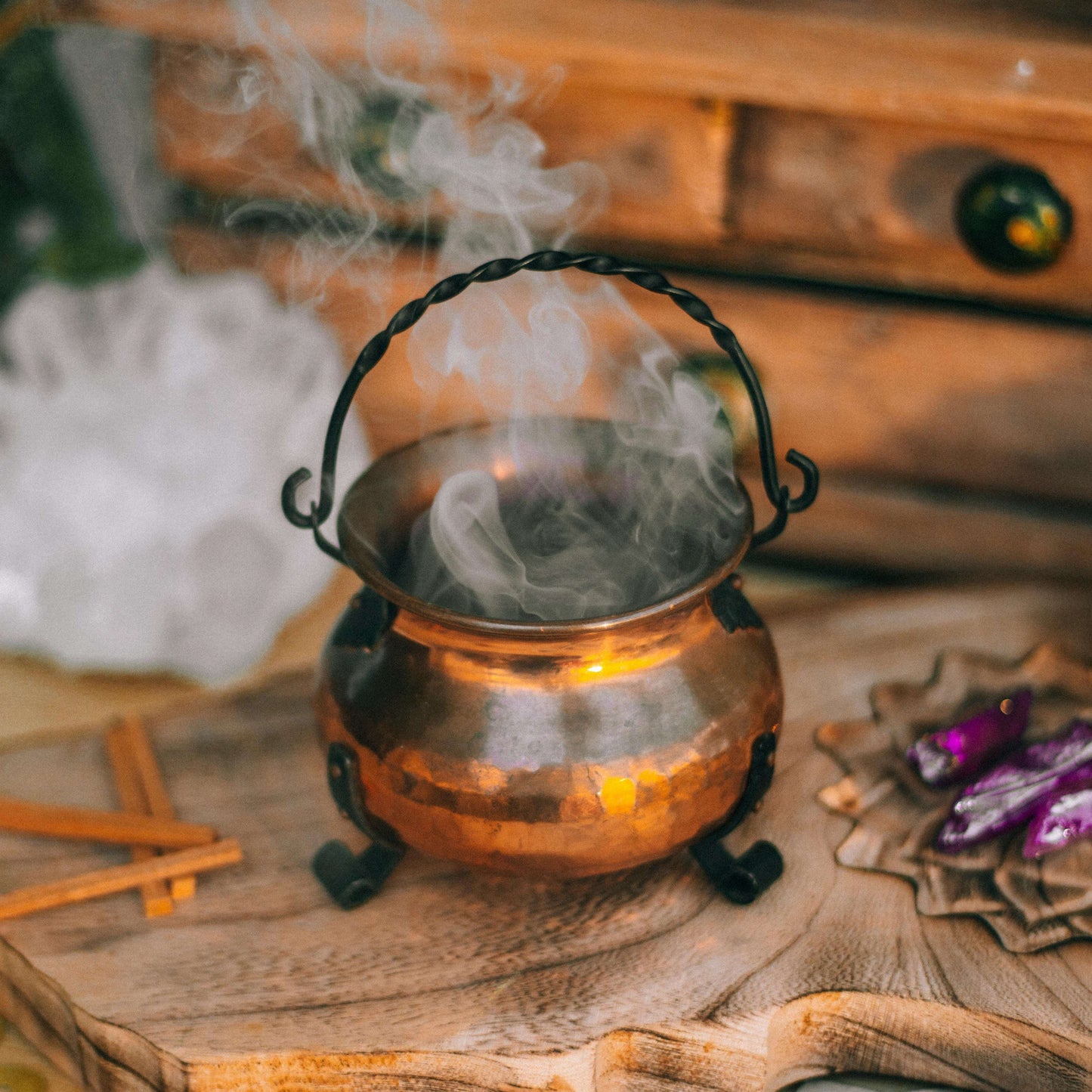 Copper cauldron with smoke on a wooden surface with mystical items.
