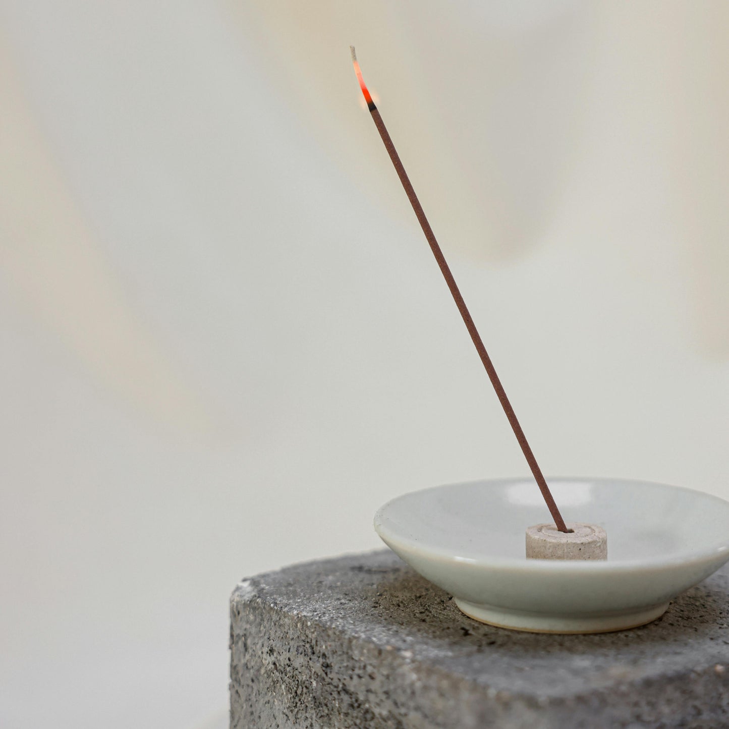 Incense stick burning in a white dish on a stone surface with a light background