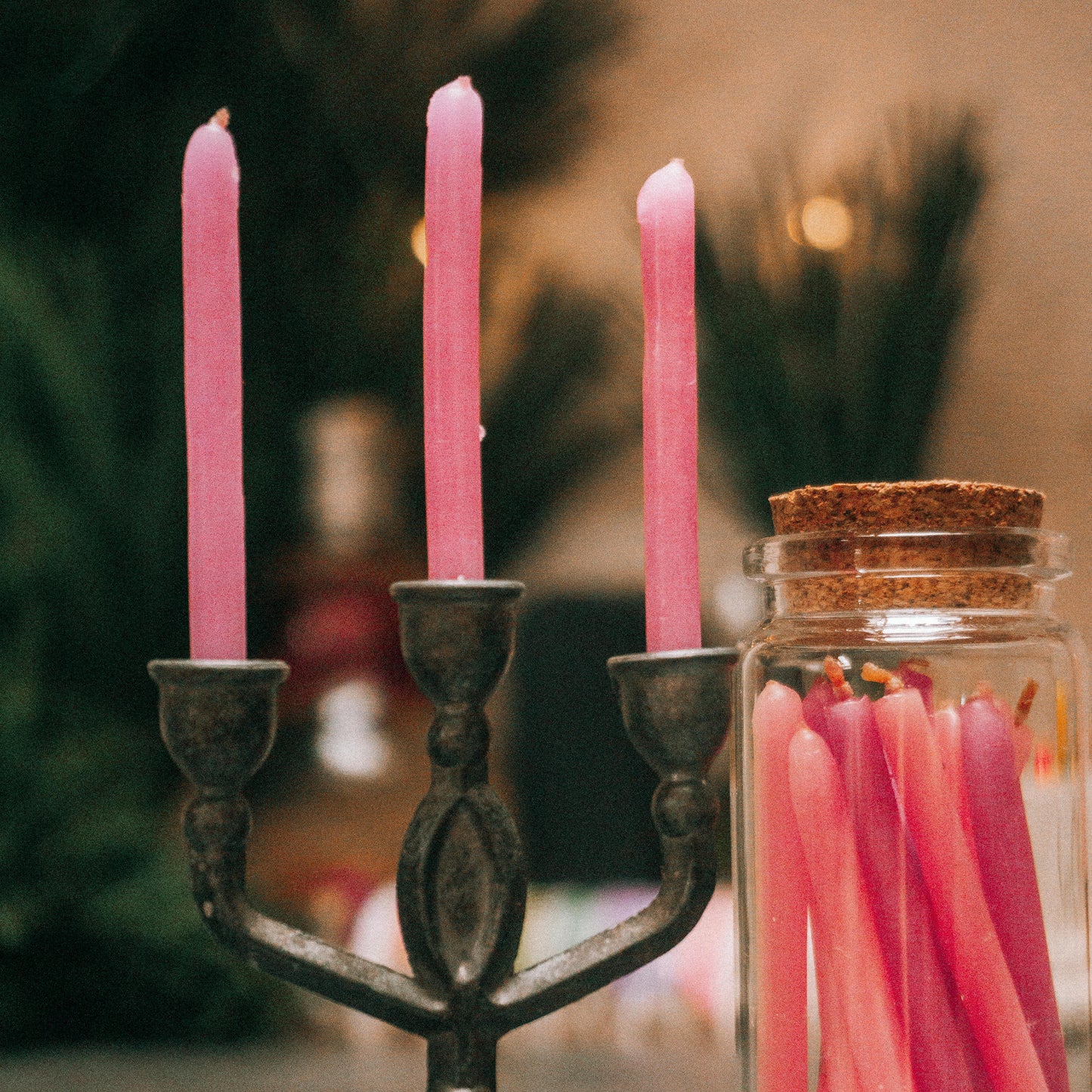 Pink candles in a metal candlestick holder with a jar of matches on a blurred background