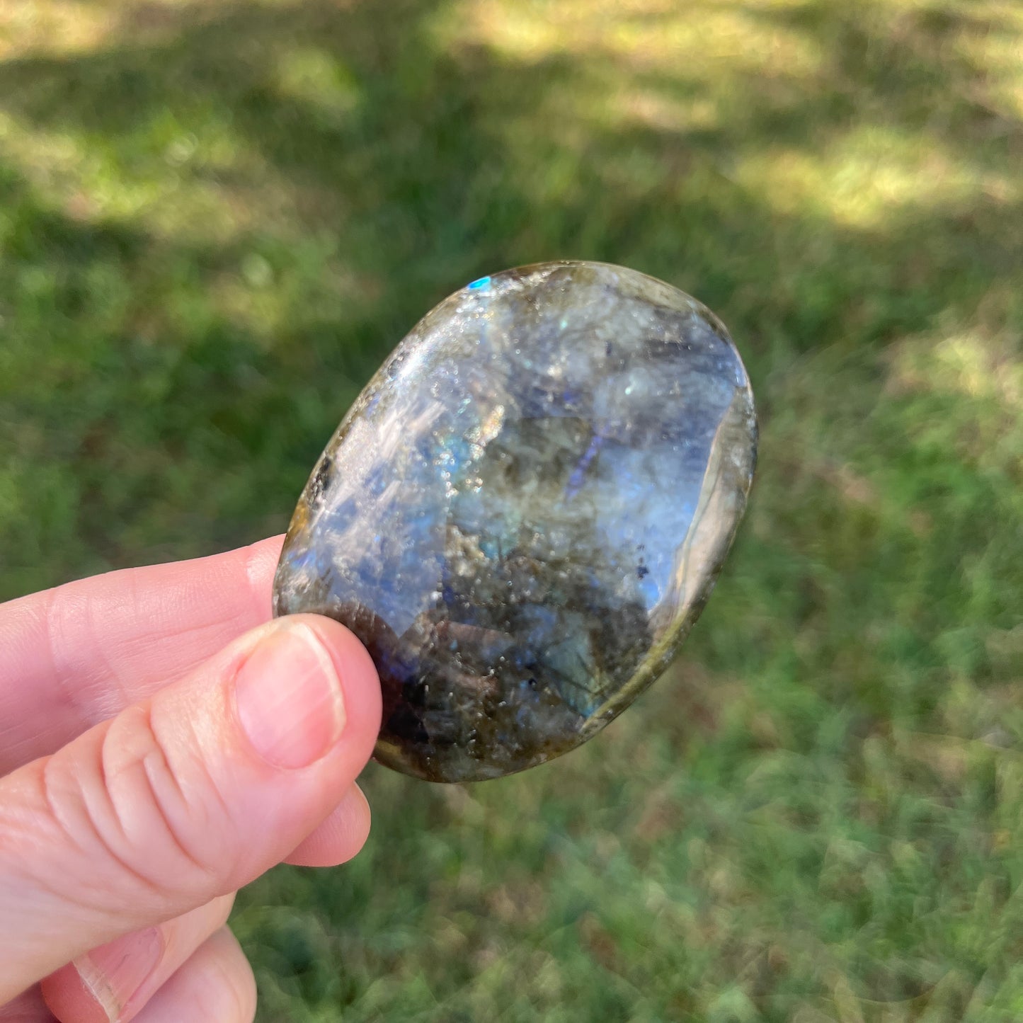 Hand holding a labradorite stone with a blurred grassy background