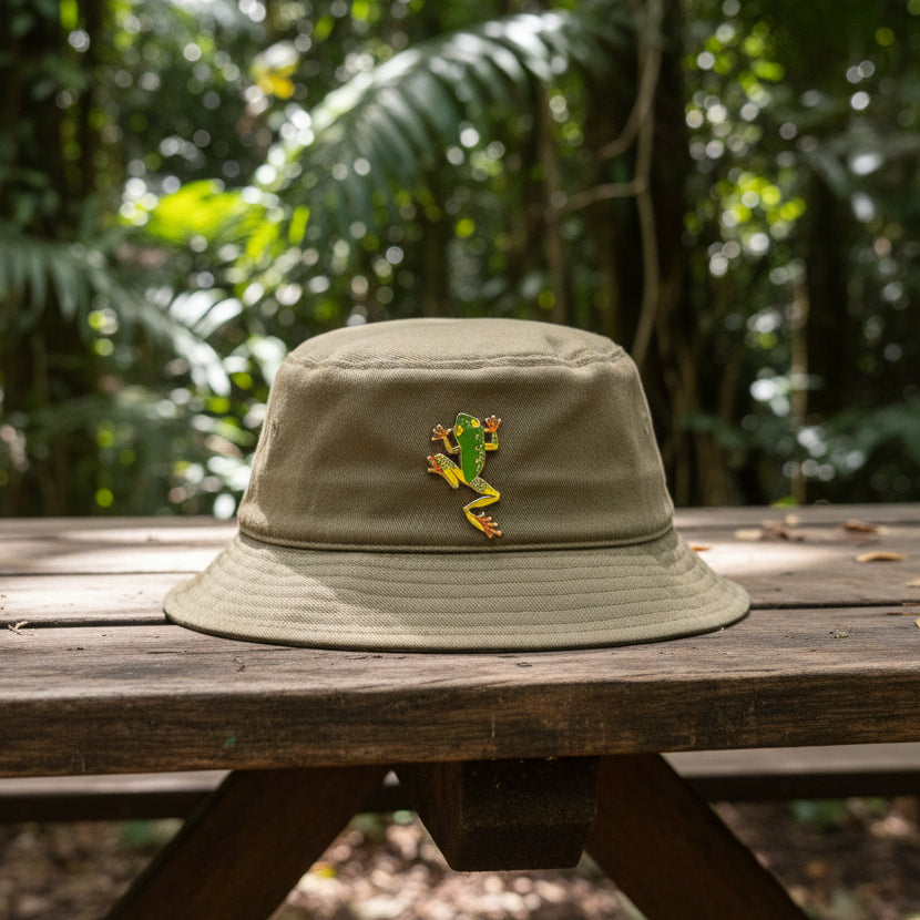 Green tree frog enamel pin on a green hat in the rainforest