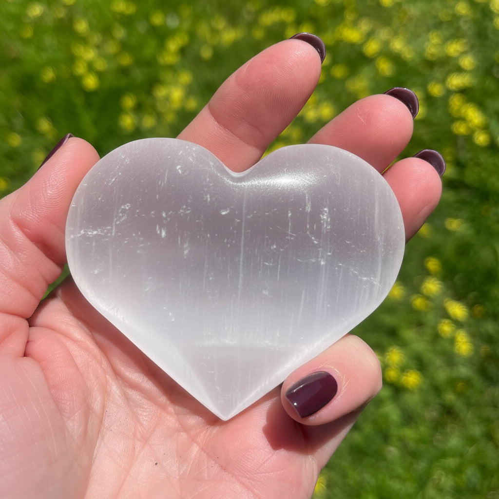 Heart-shaped crystal held in a hand with a blurred green background