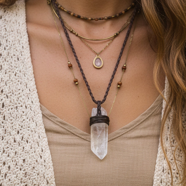 A clear quartz crystal point pendant wrapped with dark brown cord, hanging from a matching brown braided cord 