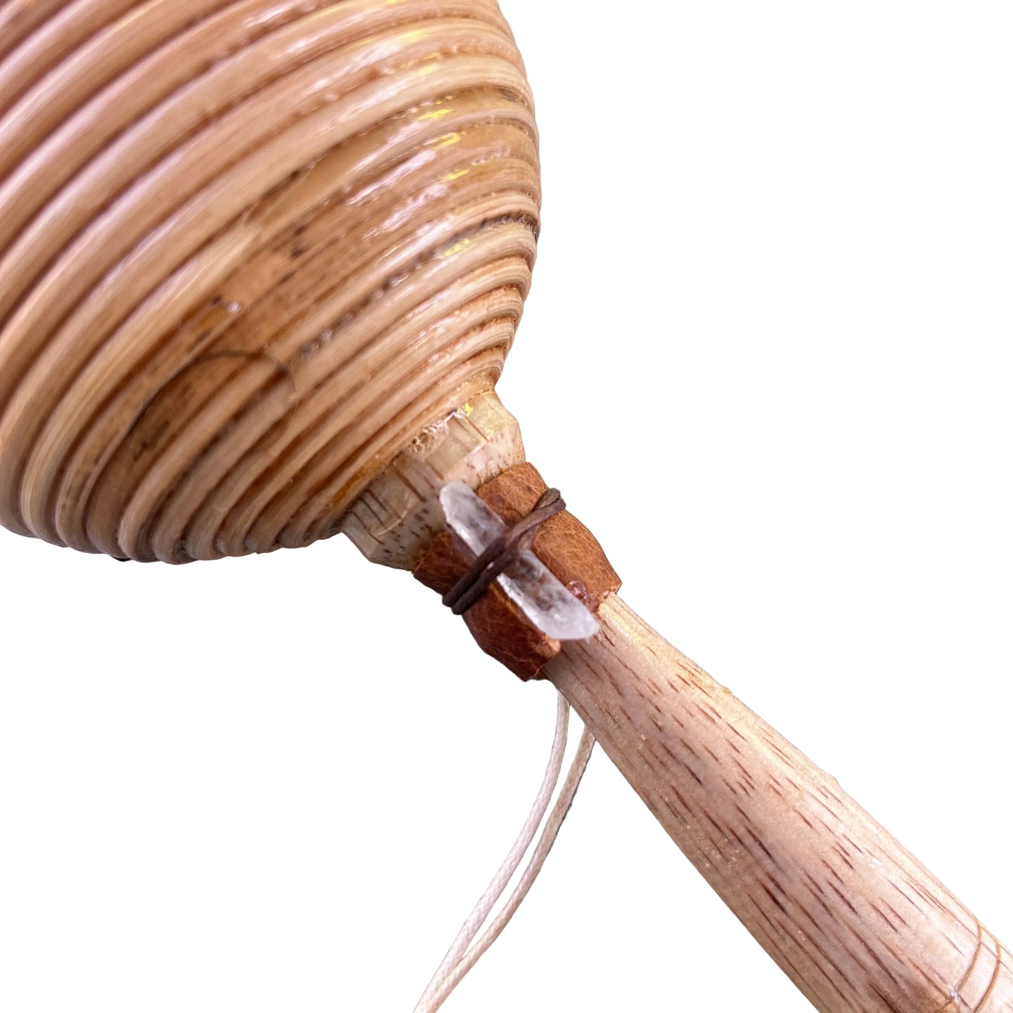 A close-up of a handmade wooden shamanic rattle shaker, a light wood handle, and a small clear crystal wrapped in brown thread, resting on a gray textured surface.