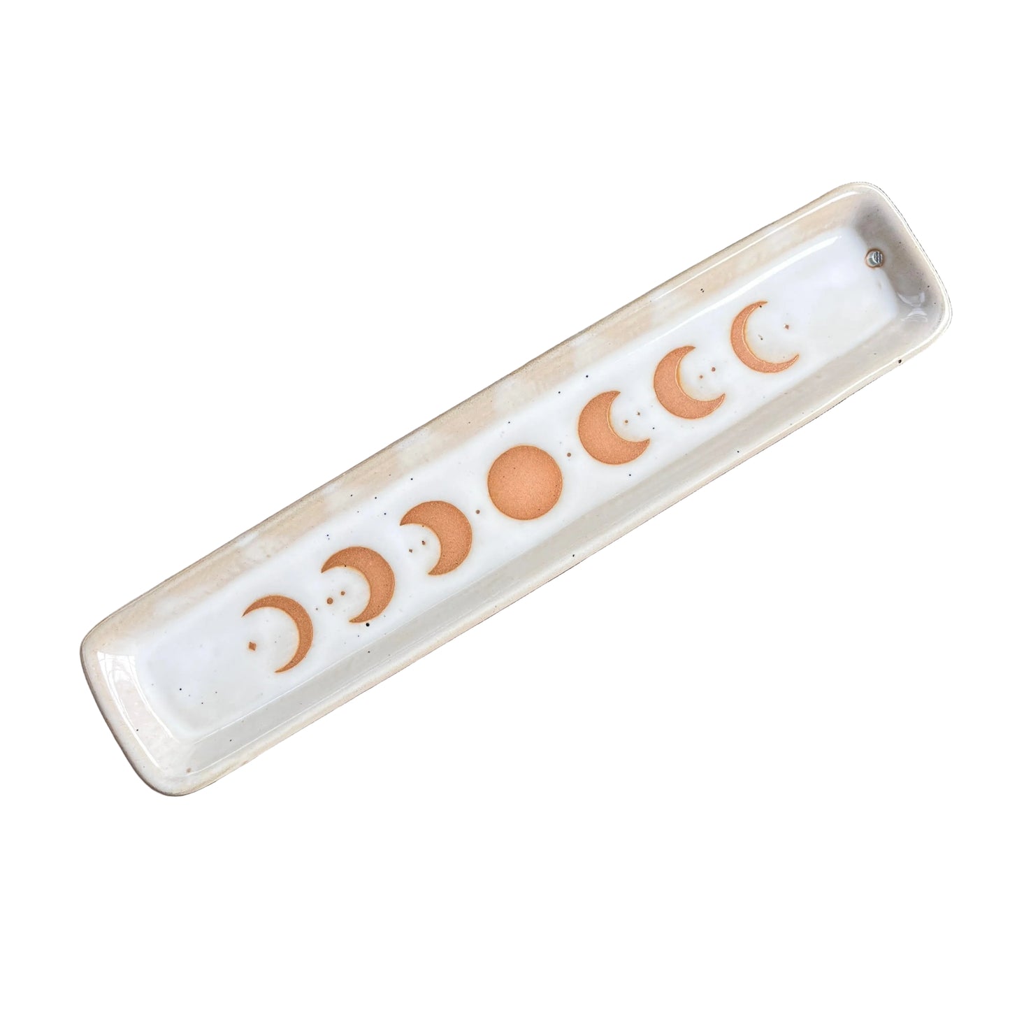 A rectangular ceramic tray with a glossy white glaze, featuring a sequence of moon phases in a warm terracotta orange color printed along the bottom. The tray is photographed diagonally on a scratched, metallic brown surface.