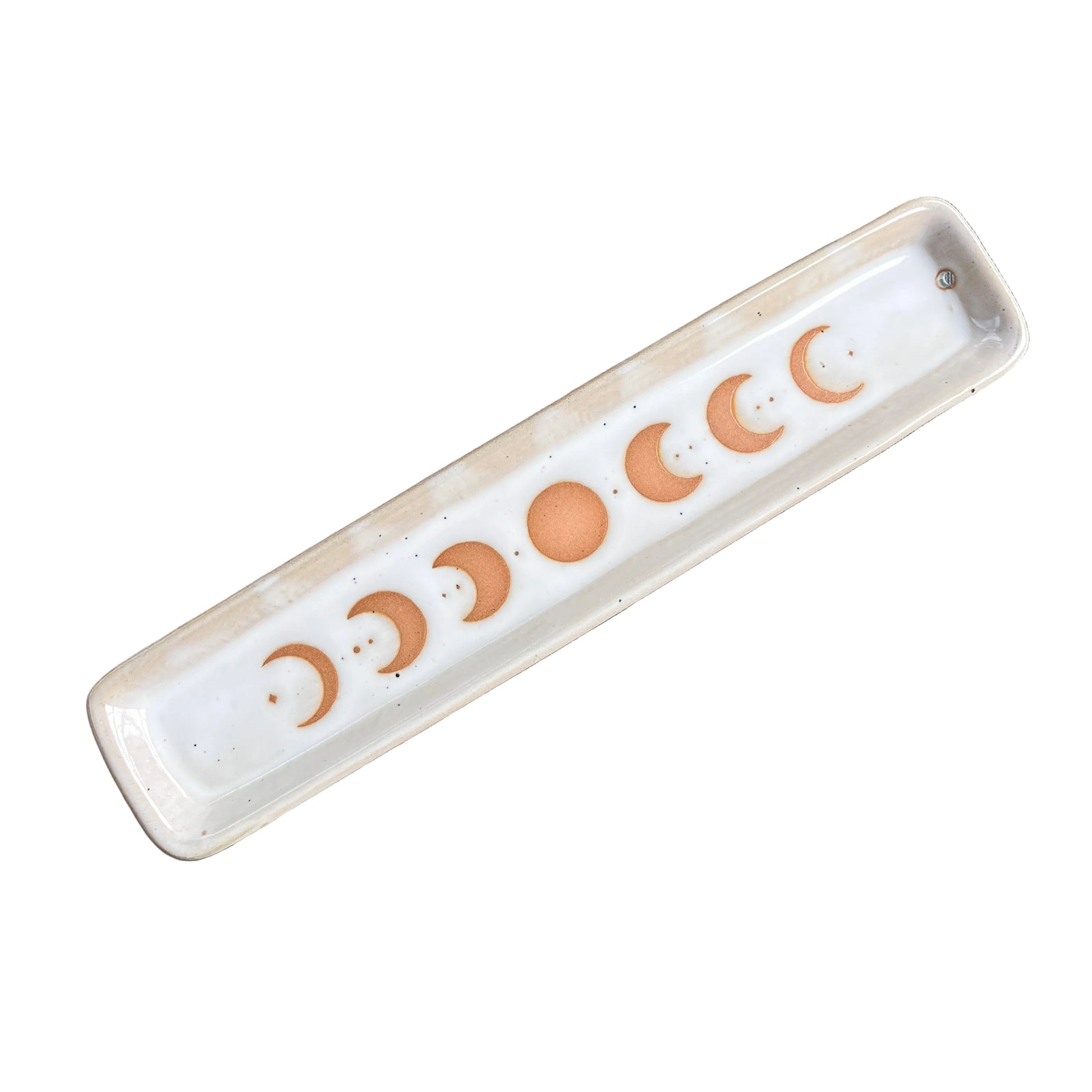 A rectangular ceramic tray with a glossy white glaze, featuring a sequence of moon phases in a warm terracotta orange color printed along the bottom. The tray is photographed diagonally on a scratched, metallic brown surface.