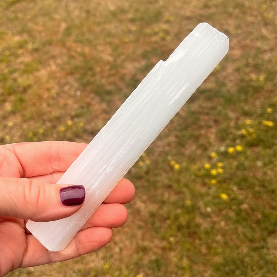 Hand holding a white selenite crystal against a grassy background