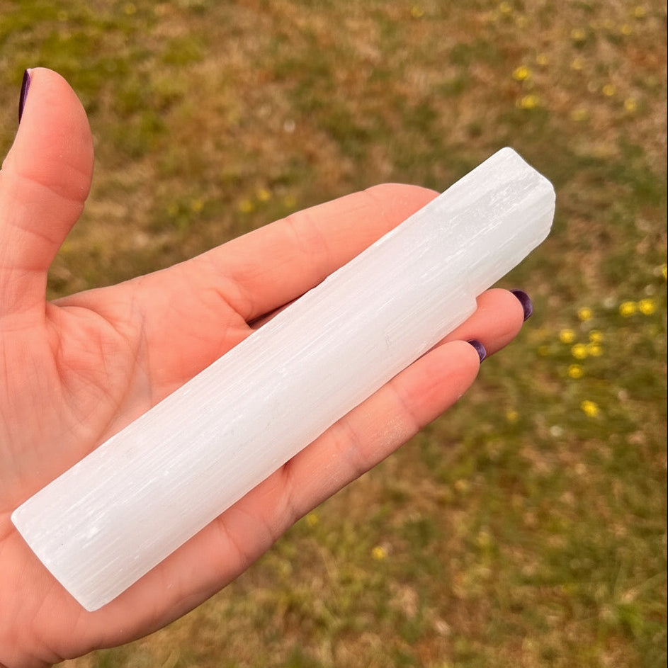 Hand holding a selenite crystal against a blurred natural background
