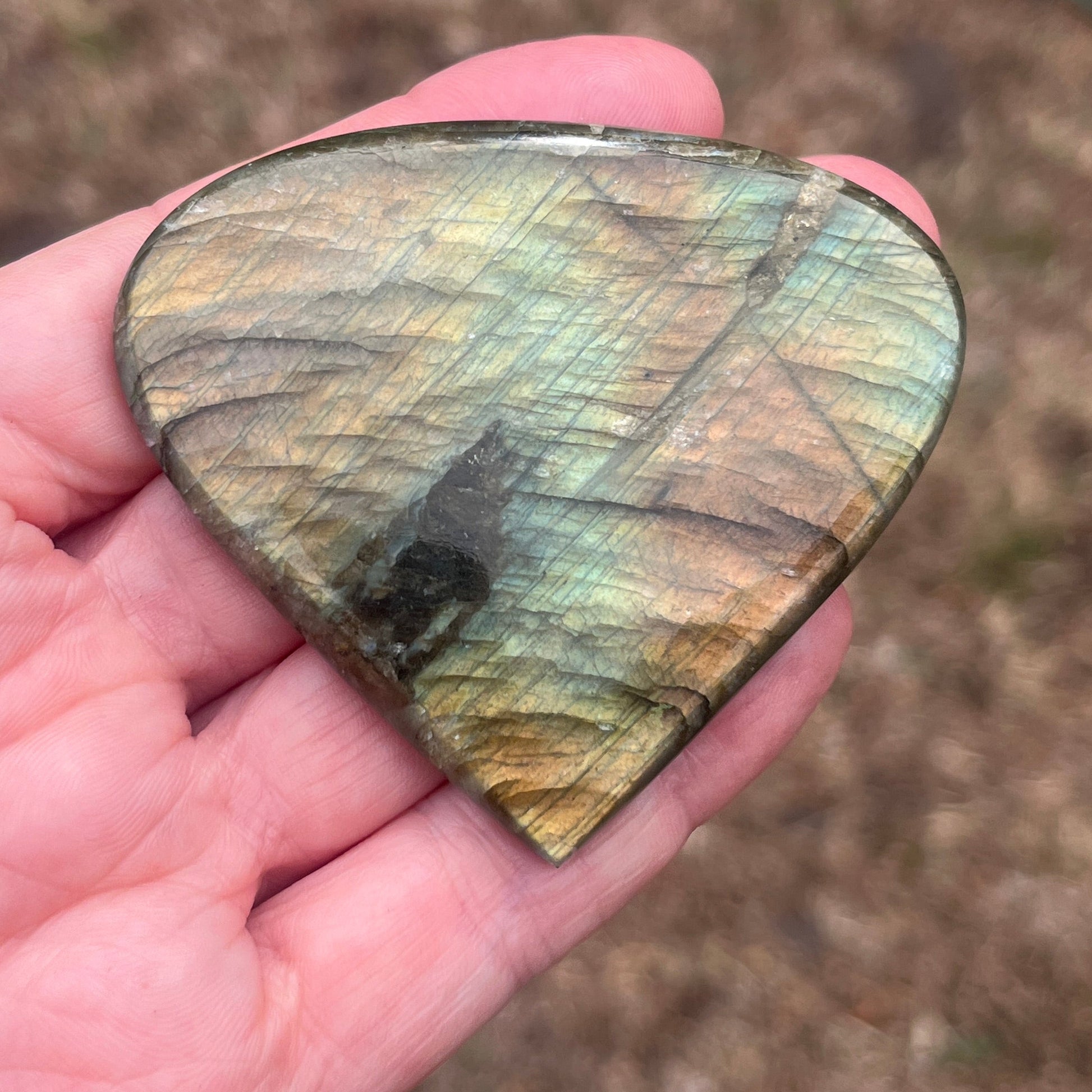 Heart-shaped labradorite stone held in a hand with a blurred natural background
