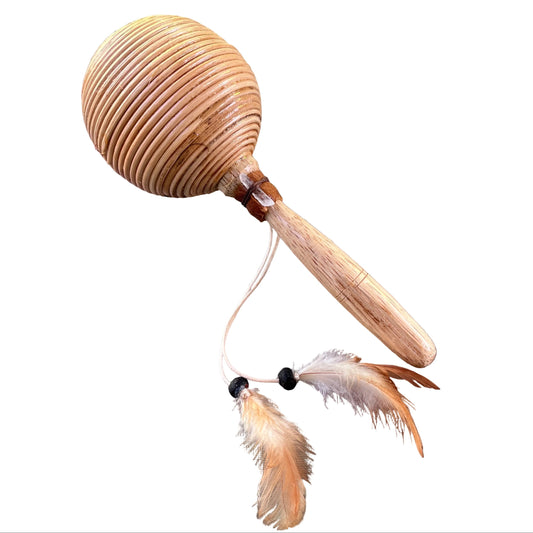 A wooden maraca or shamanic shaker with a ribbed oval head, a light wood handle, and two hanging feathers attached by white cords with black beads