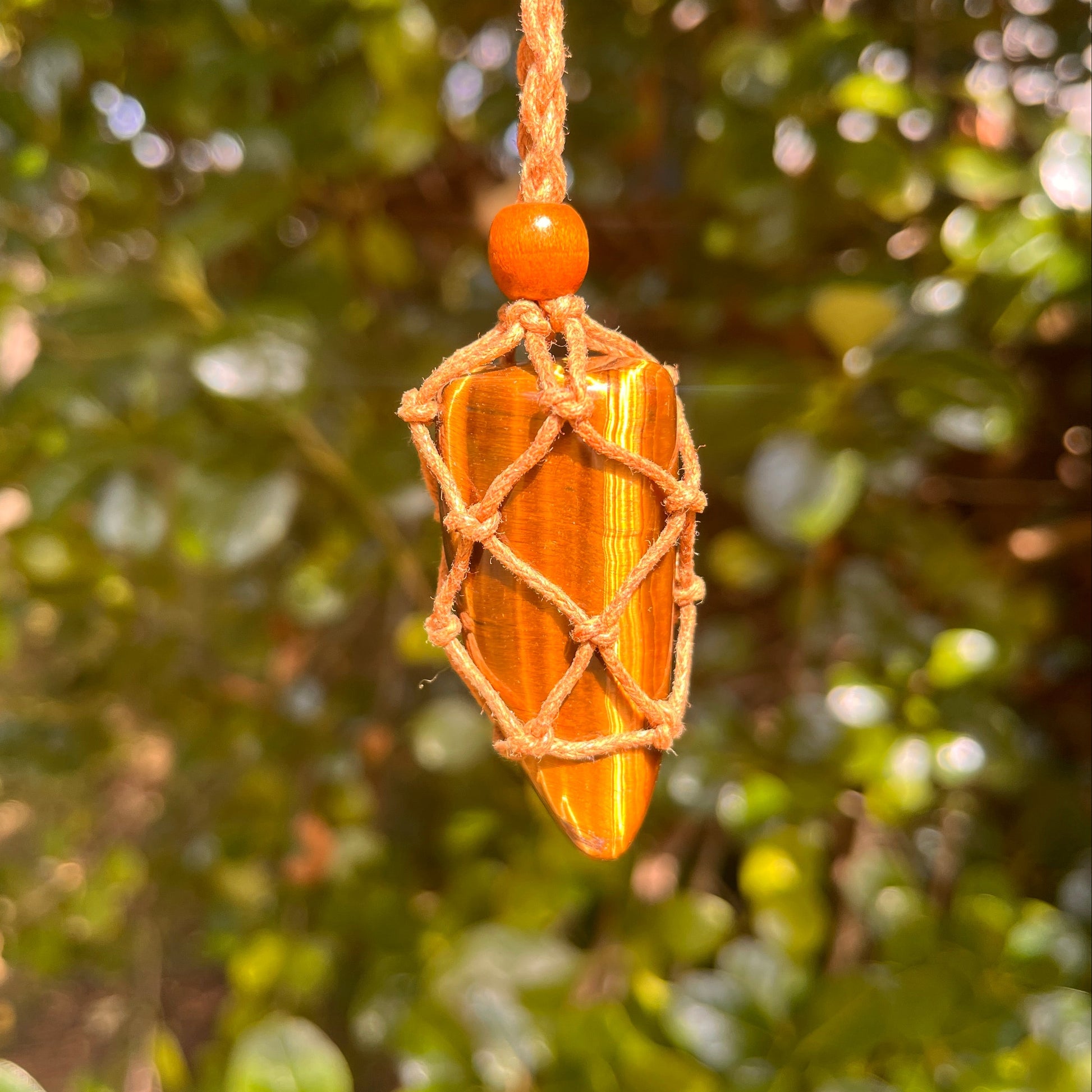 Macrame Tigers Eye crystal necklace against a blurred green foliage background