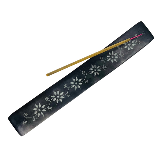 Black incense holder with floral designs and two incense sticks on a white background