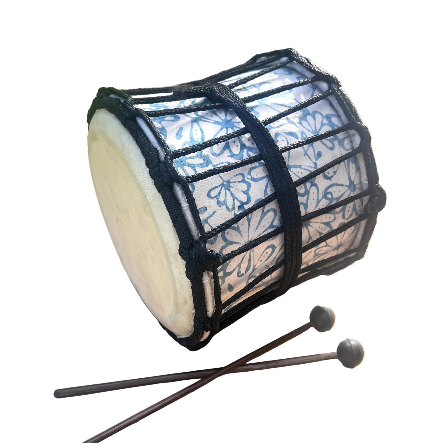 A hand drum with a white drumhead, blue floral patterned body, and black rope tensioning, shown outdoors with two mallets.