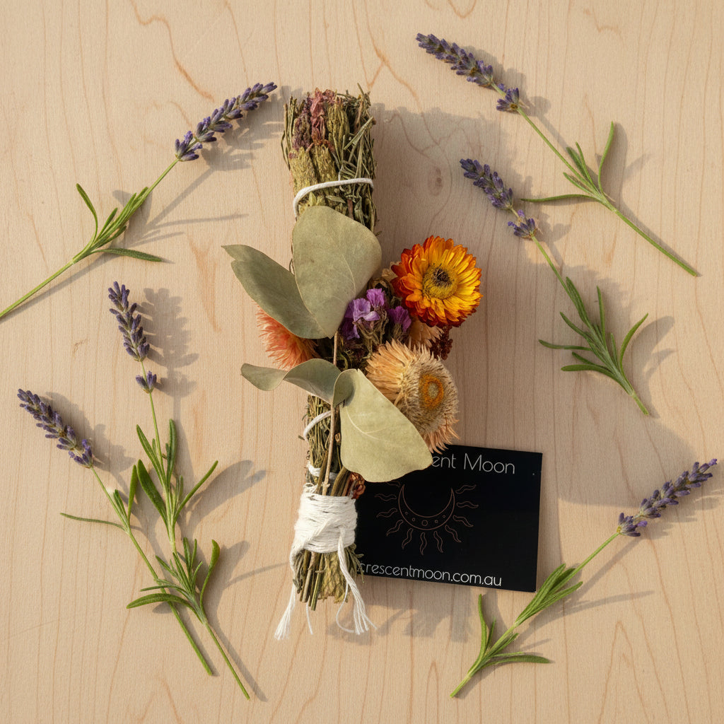 A dried flower and herb bundle tied with white string, featuring sage green leaves, an orange daisy, purple dried flowers, 