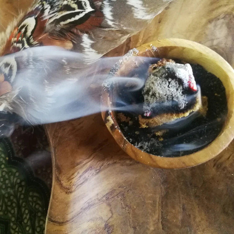Tribe Earth Incense burning in a wooden bowl with smoke rising on a wooden surface.