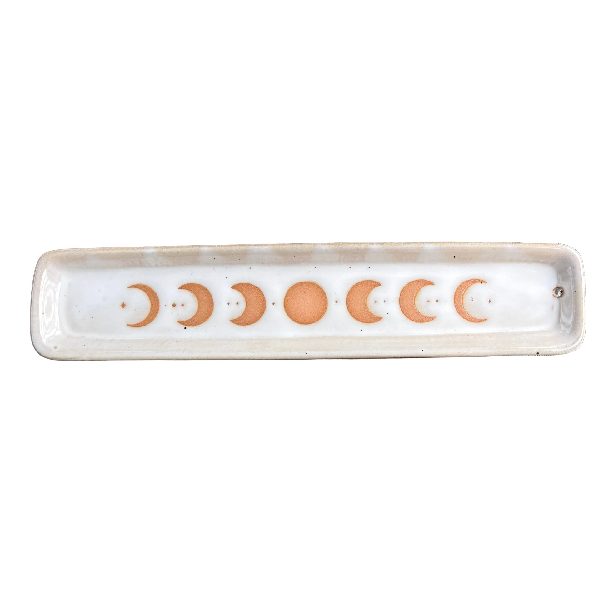 A rectangular ceramic dish with a white glaze featuring a row of seven orange moon phases, including a full moon in the center, displayed on a scratched brown glass surface.
