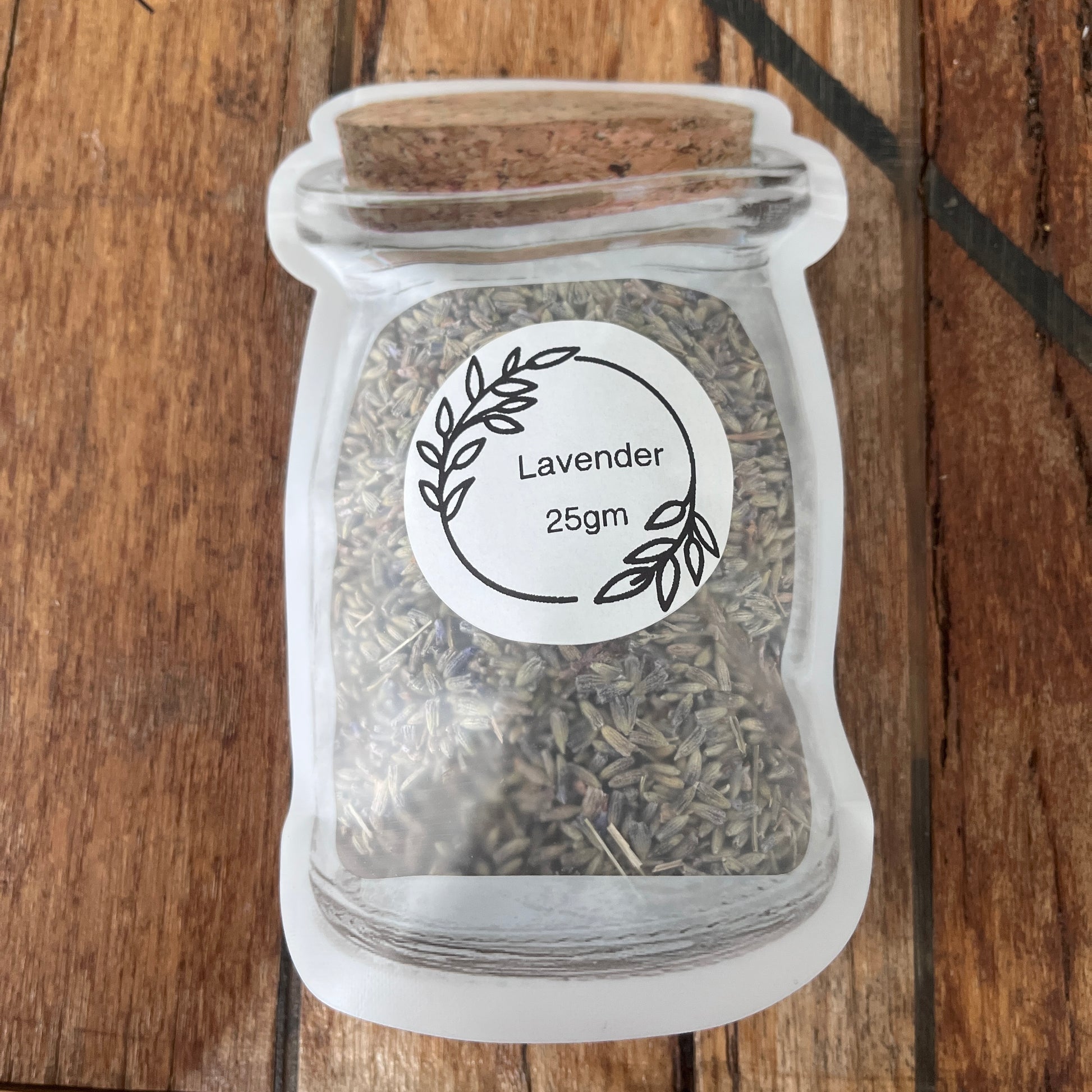 A small clear packet, filled with dried lavender buds, and labeled 'Lavender 25gm' on a wooden surface.