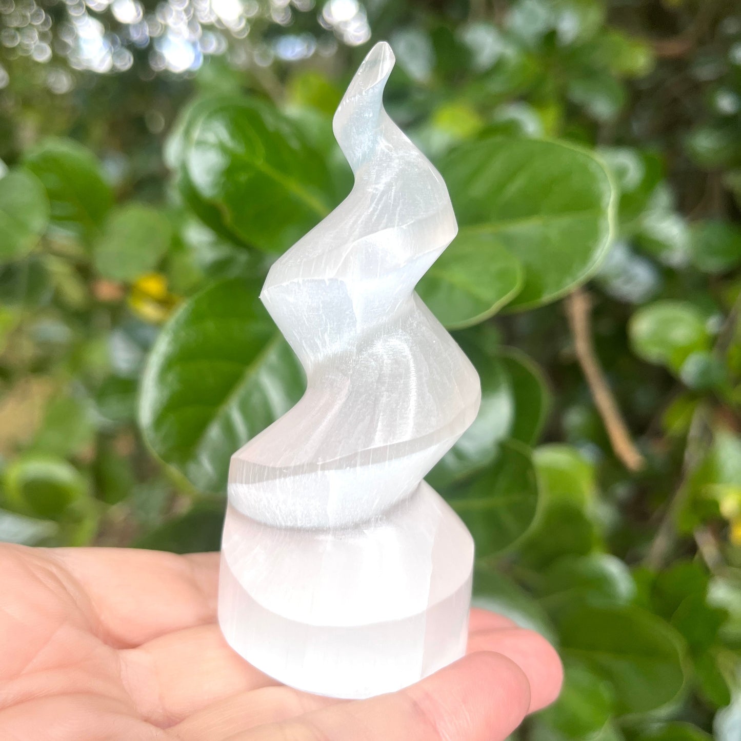 Selenite spiral tower held in a hand with a green leafy background