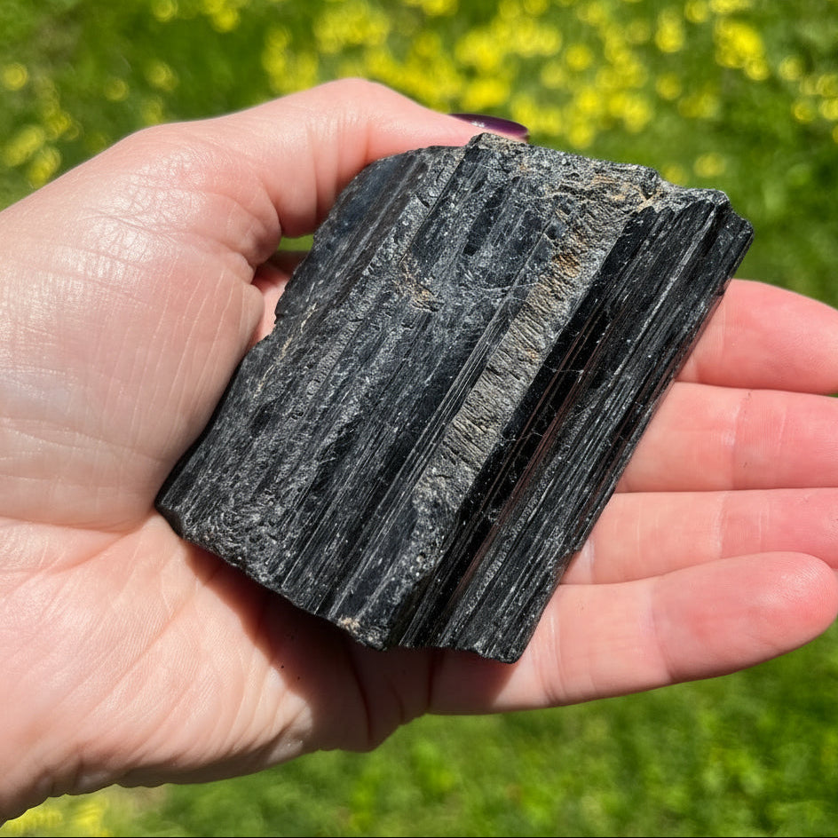 Hand holding a piece of black stone with a blurred green and yellow background