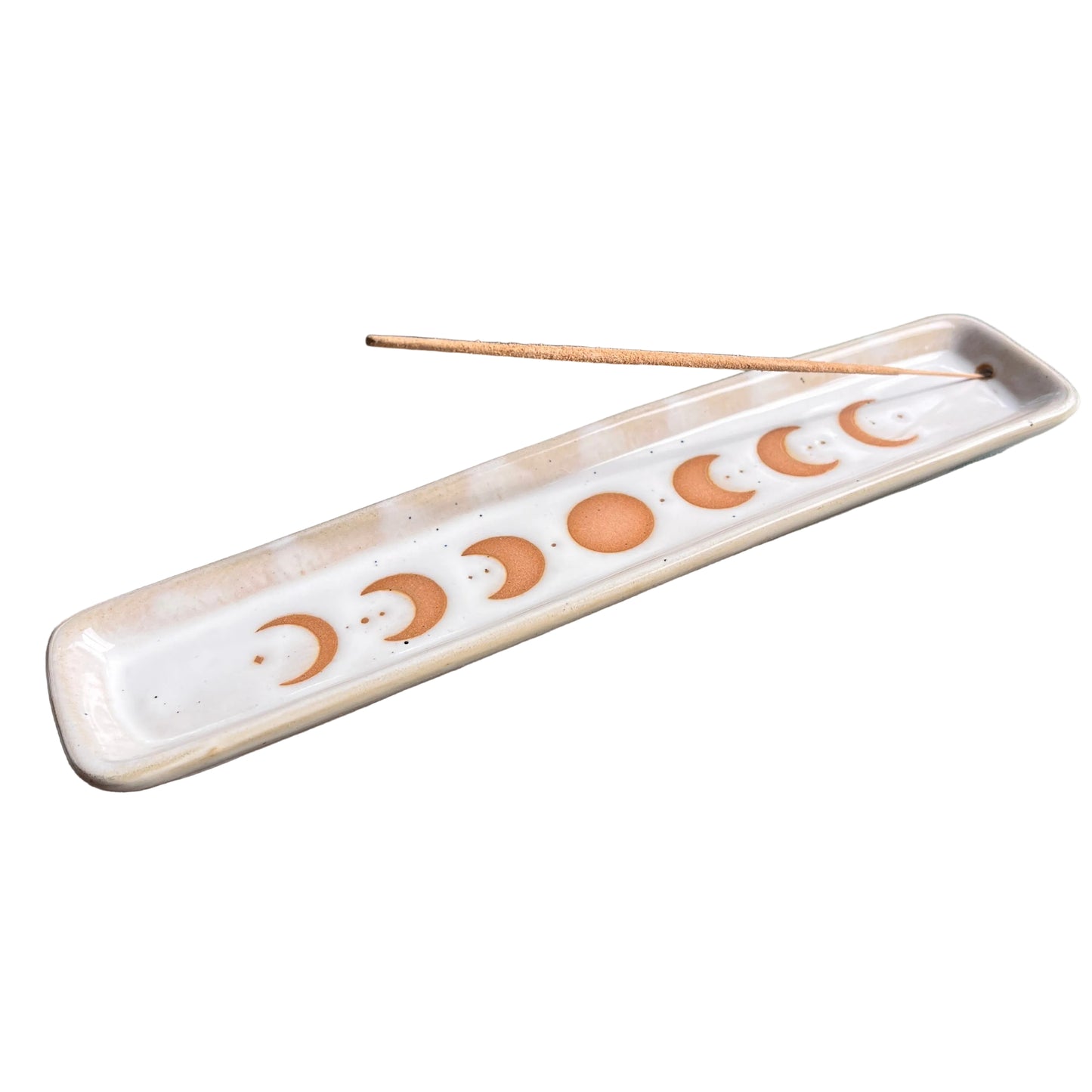 A rectangular ceramic incense holder with a moon phase design, containing a single incense stick, resting on a dark textured surface.