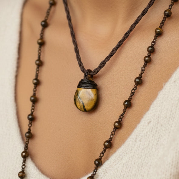 A small pendant necklace with a carved yellow stone featuring dark brown veining, suspended from a dark brown braided cord, 