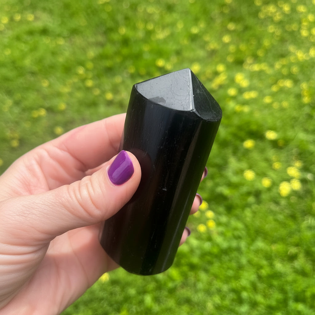 Hand holding a black crystal against a green grass background