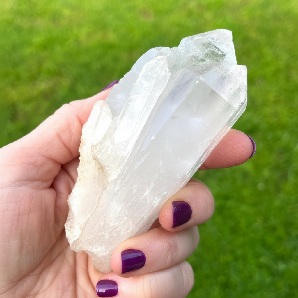 Hand holding a clear quartz crystal against a grassy background