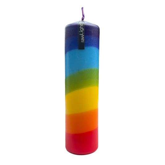 Colorful cylindrical candle with rainbow pattern on a white surface, blurred outdoor background