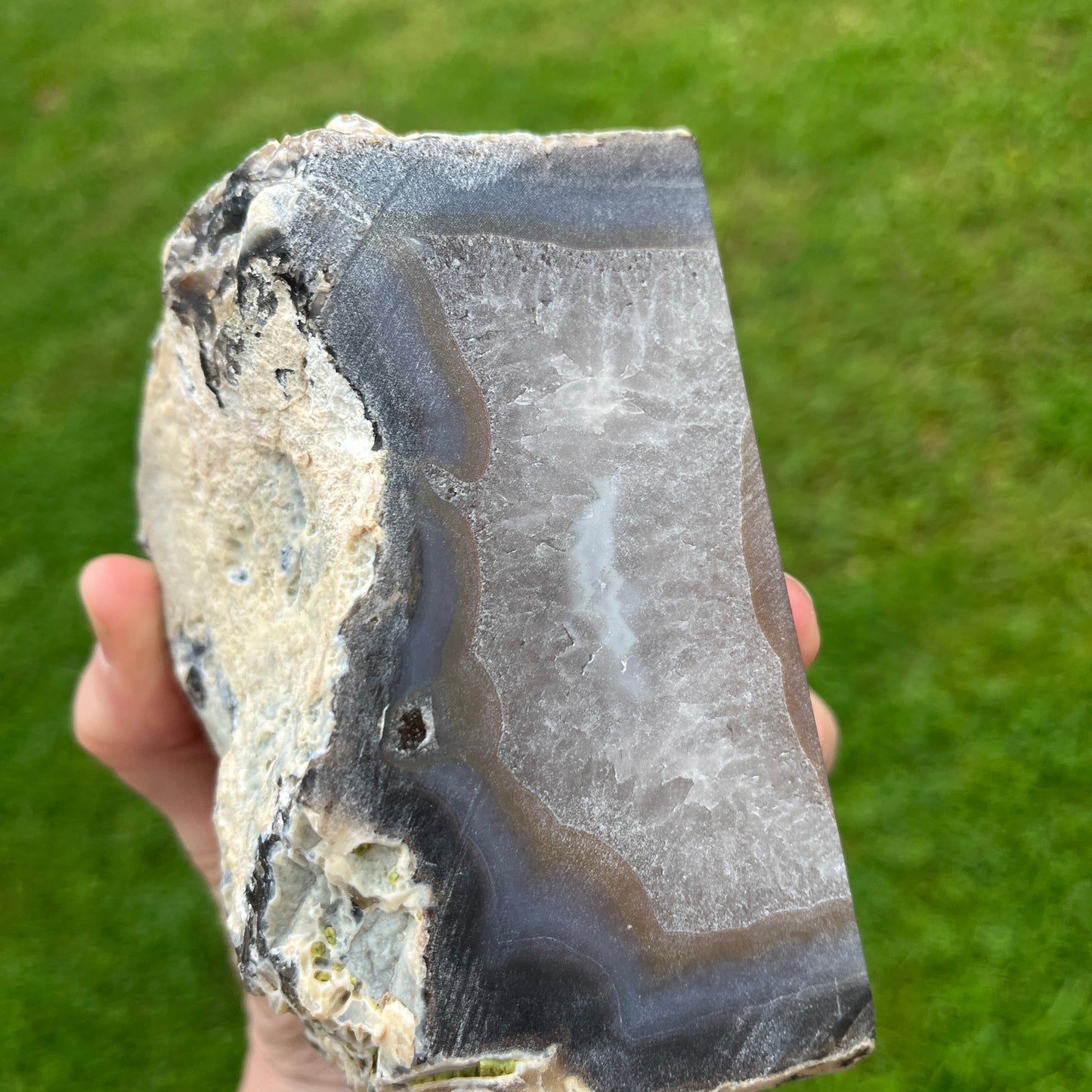 Hand holding a rough stone with a green grass background
