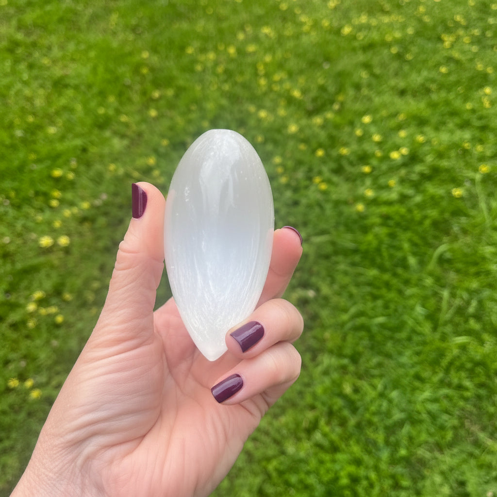 Hand holding a selenite heart against a grassy background