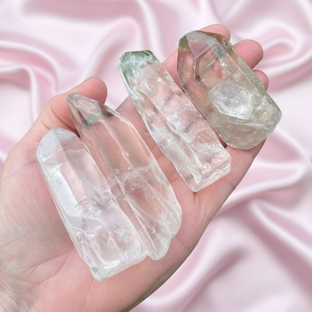 Hand holding four clear quartz crystal points against a pink background