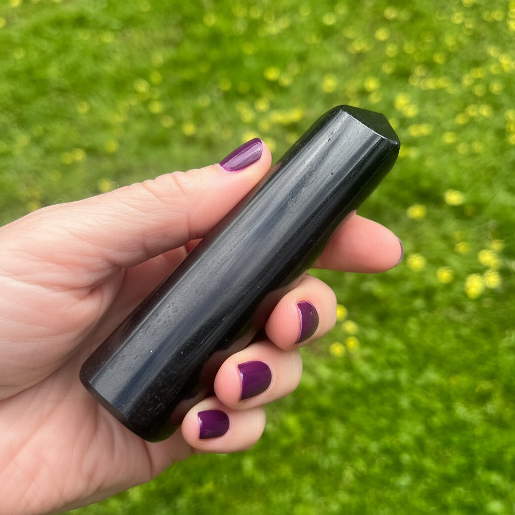 Hand holding a black tourmaline tower against a green grass background