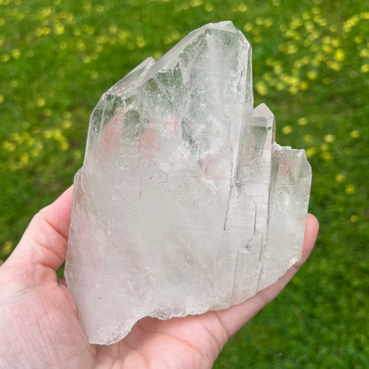 Clear crystal held in a hand with a blurred green outdoor background
