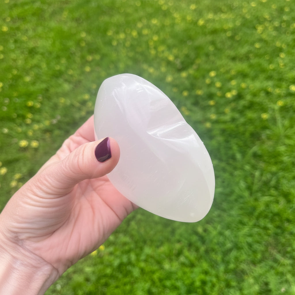 Hand holding a selenite crystal heart against a grassy background
