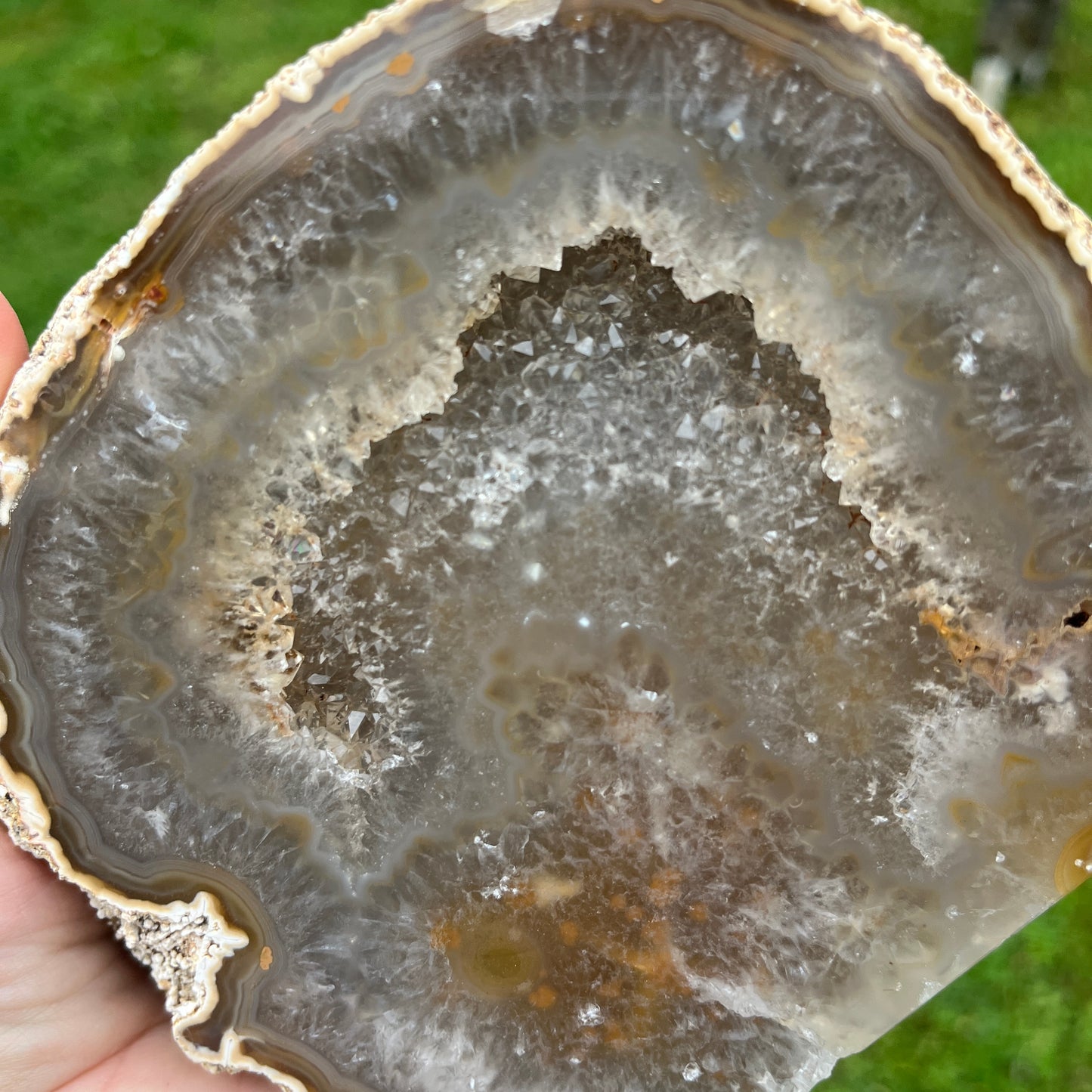 Close-up of a geode with layered crystal structure held by a hand against a green background