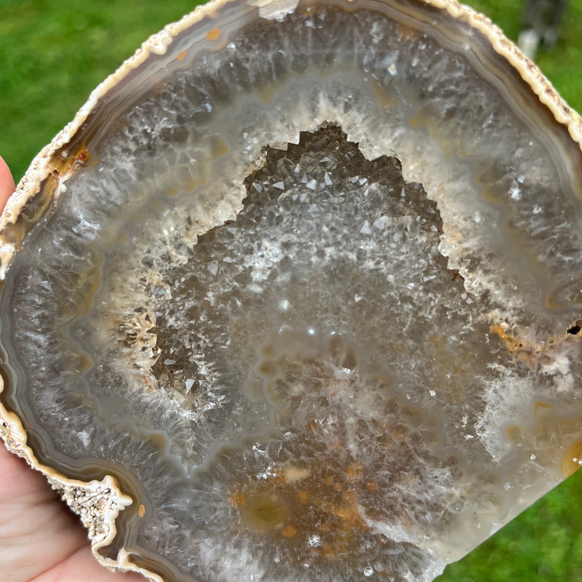 Close-up of a geode with layered crystal structure held by a hand against a green background