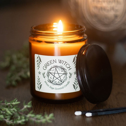 Candle in a jar with a 'Green Witch' label on a wooden surface with greenery.
