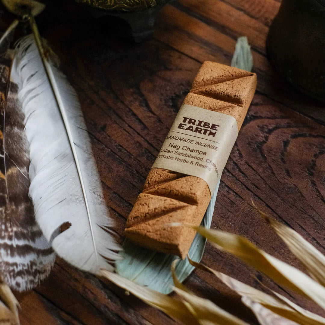Incense sticks with a 'Tribe Earth' label on a wooden surface with feathers and plants.