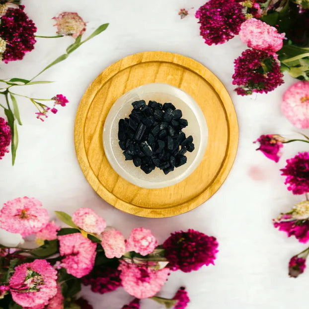 Black tourmaline crystals in a bowl surrounded by pink and purple flowers on a white background
