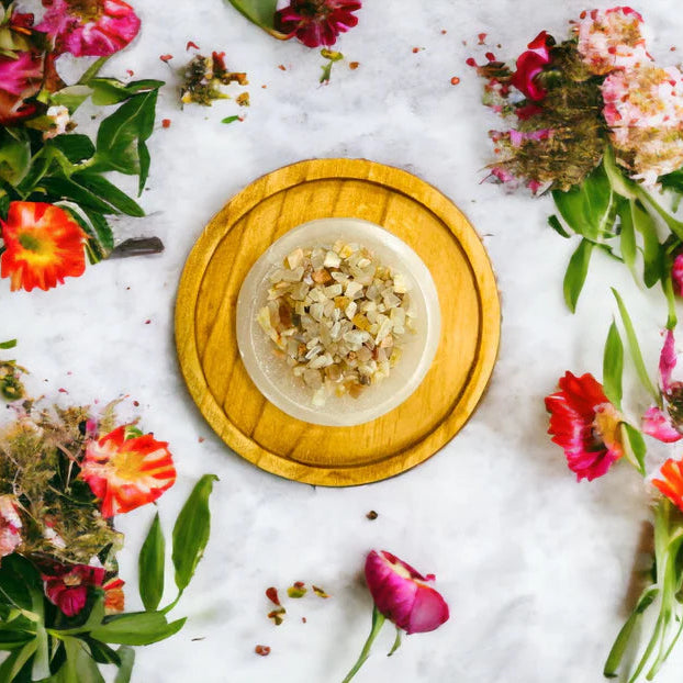 Peach moonstone crystals on a wooden plate surrounded by colorful flowers on a white background