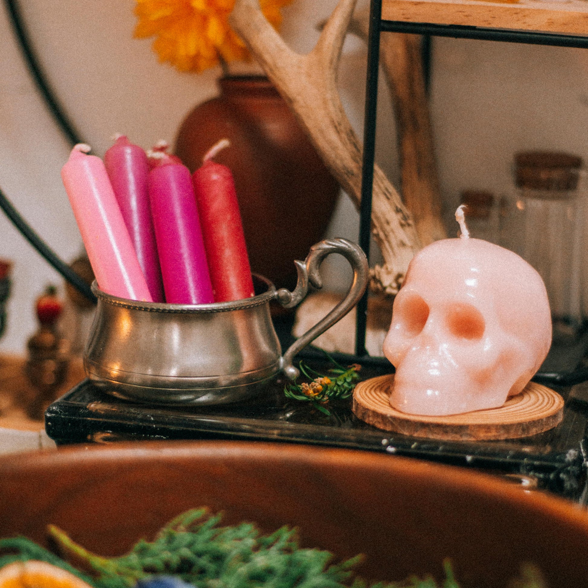 Decorative setup with pink candles, skull-shaped candle, and herbs on a table.
