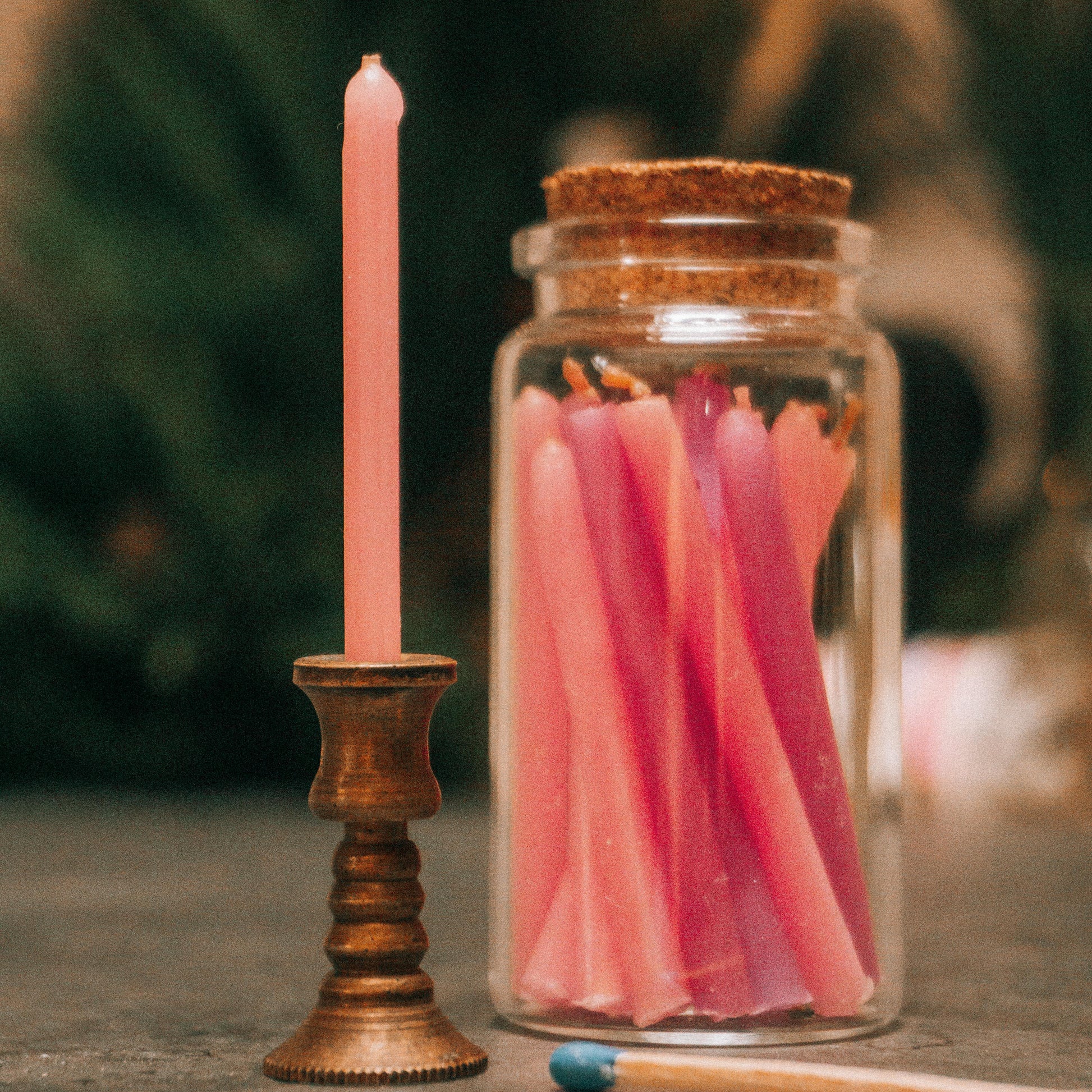 Pink candle in a wooden holder with a jar of pink candles and a match on a blurred background