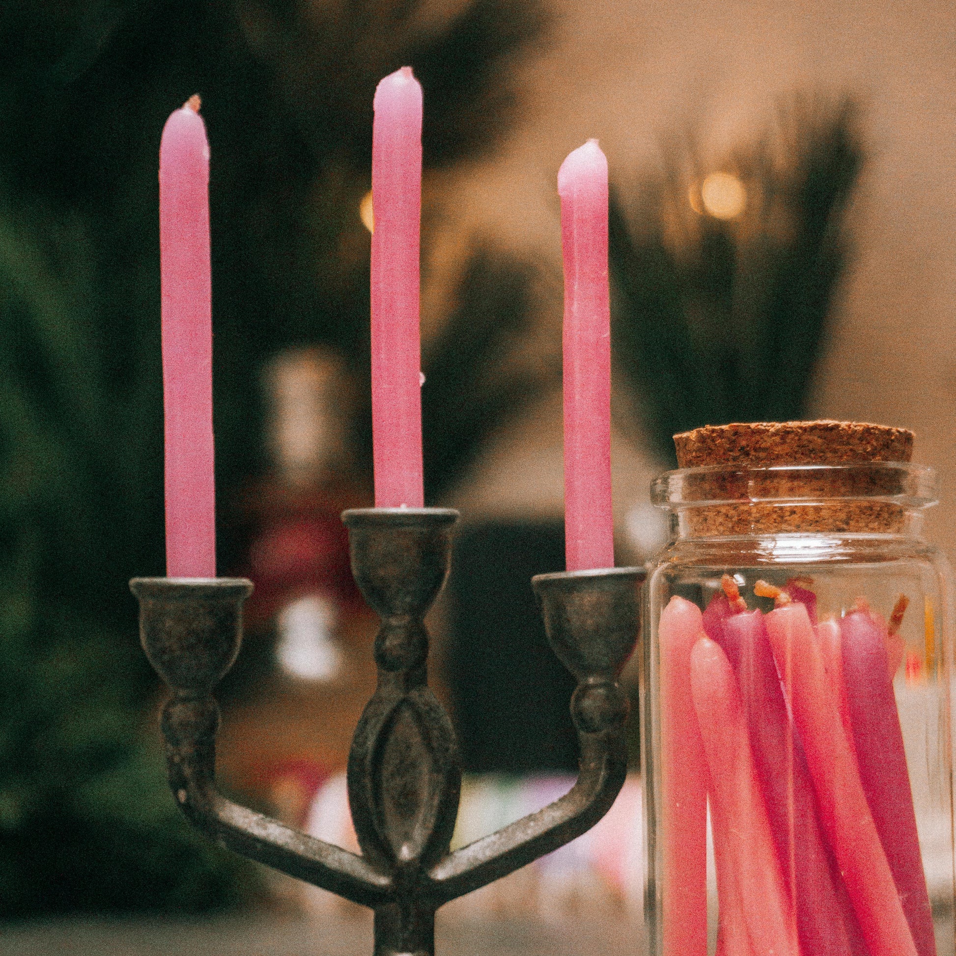 Pink candles in a metal candlestick holder with a jar of matches on a blurred background