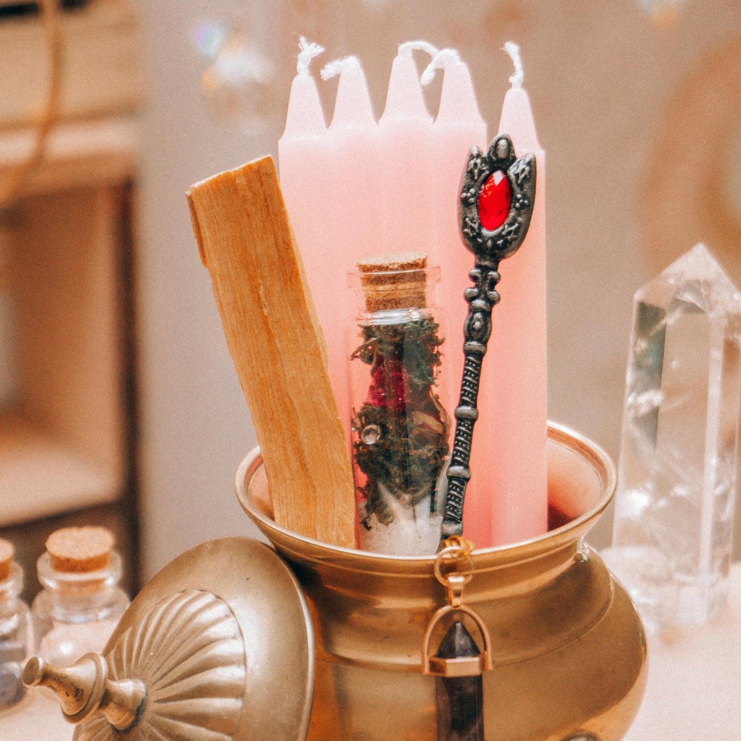 Decorative setup with pink candles, a wooden stick, and a small jar in a brass container.