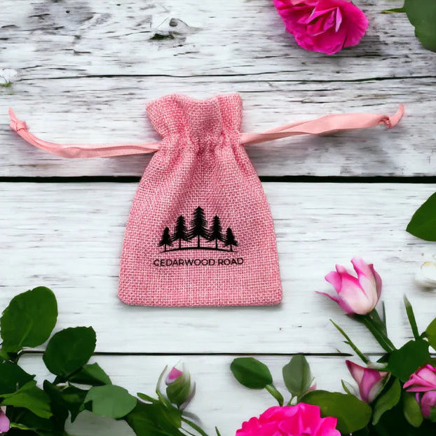 Pink drawstring bag with 'Cedarwood Road' logo on a wooden surface with pink flowers.