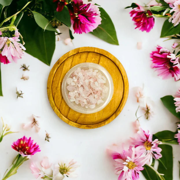 Wooden bowl with a rose quartz crystals surrounded by pink and green flowers on a white background